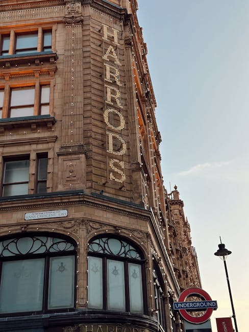 An exterior view of a historic, ornate building in Knightsbridge, featuring detailed stonework and decorative domes on the roof, with the name 'Harrods' displayed on a vertical sign attached to the fa