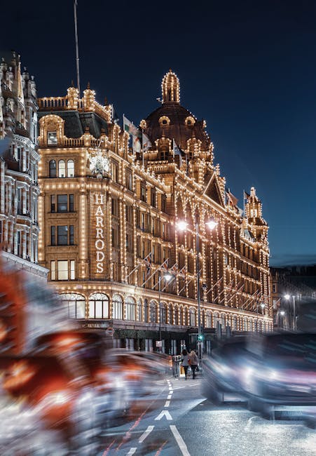 A nighttime street scene in Knightsbridge featuring a large, historic building illuminated with numerous decorative lights outlining its architectural features, including domes and turrets. The building has a sign displaying 